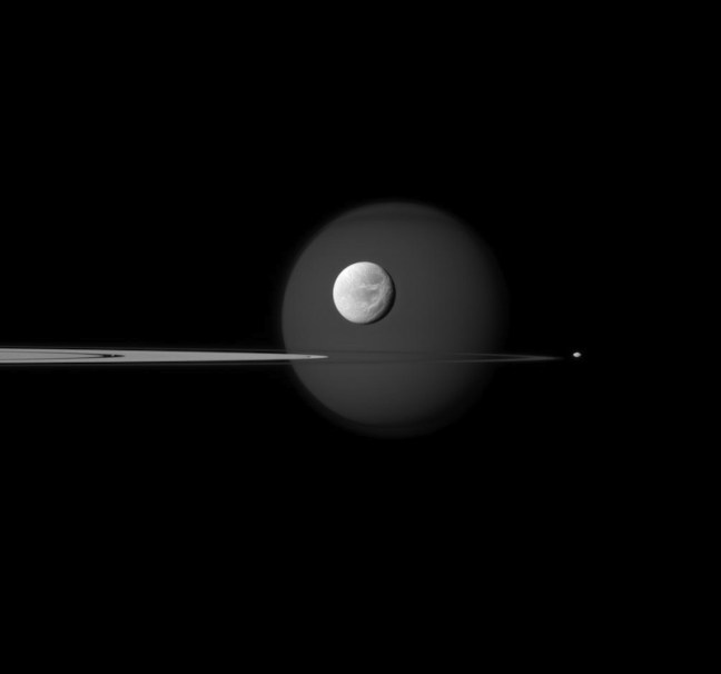 Dione, con Titán al fondo captado por la Cassini a fotografiada por Cassini a 2 millones de km de distancia. Créditos: NASA/JPL.