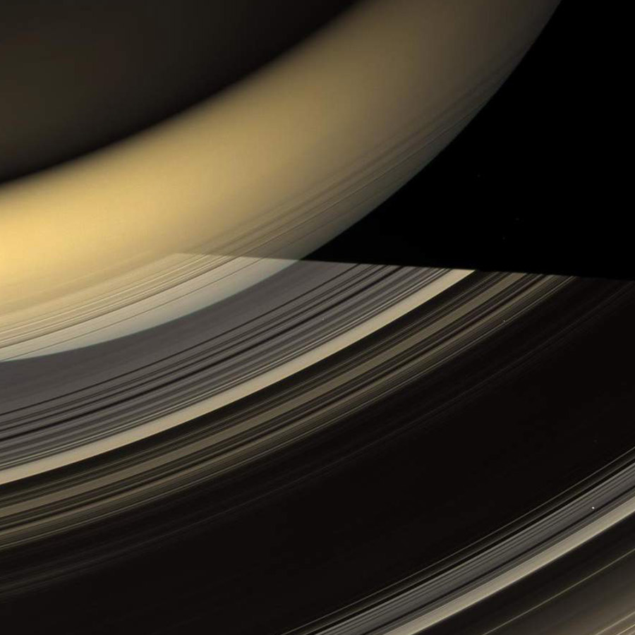 Los anillos de Saturno vistos en perspectiva con el planeta parcialmente iluminado en el fondo