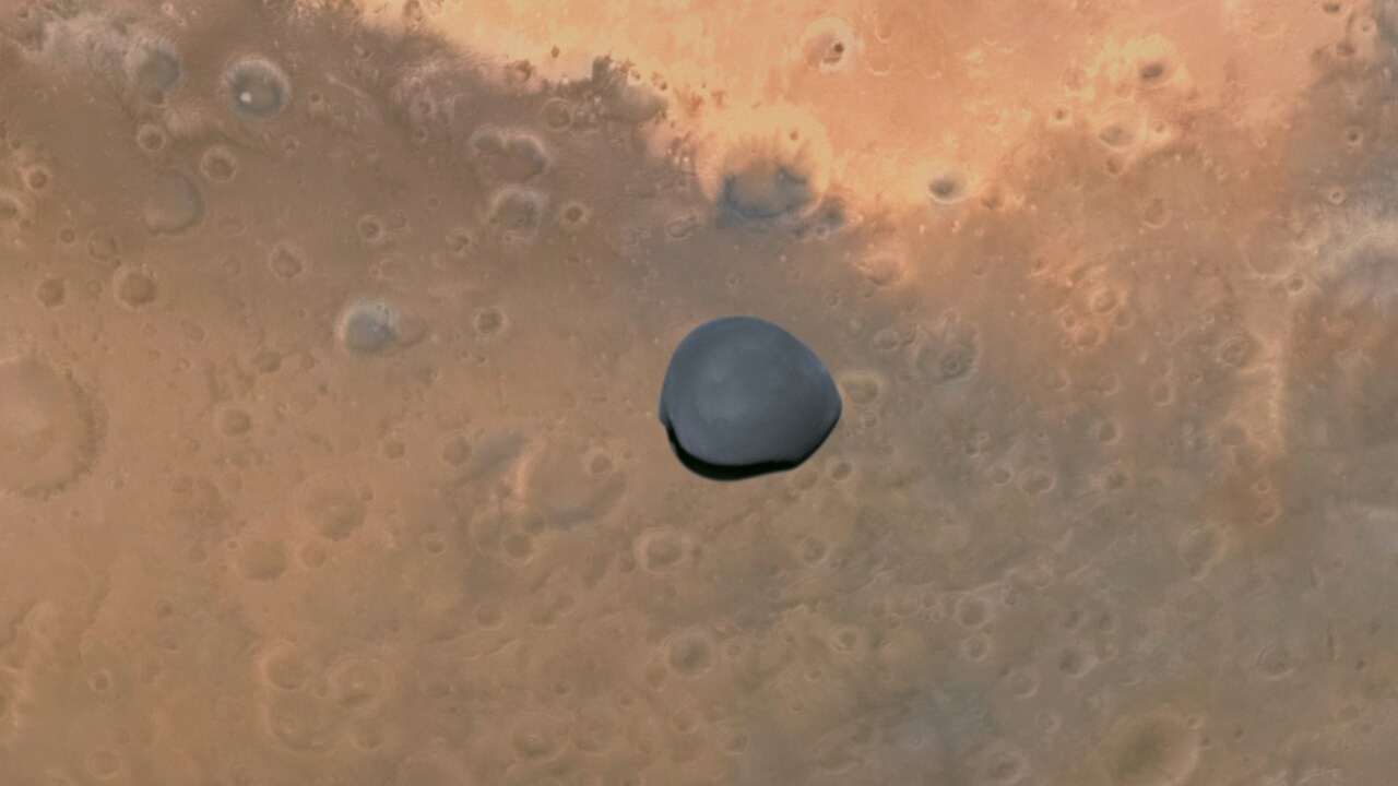 Deimos fotografiado por la cámara AFC de Hera durante el sobrevuelo del 12 de marzo de 2025, con la superficie de Marte al fondo.