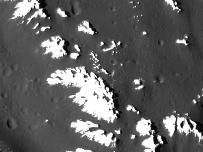 Cumbres brillantes cubiertas de escarcha en el anillo exterior de la cuenca de impacto Asgard en Calisto, sobre llanuras oscuras y craterizadas.