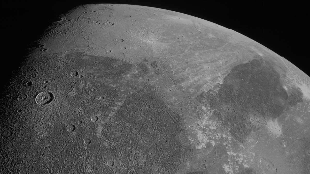Superficie de Ganímedes vista por JunoCam, con cráteres y extensas regiones de terreno oscuro y surcado iluminadas en el terminador