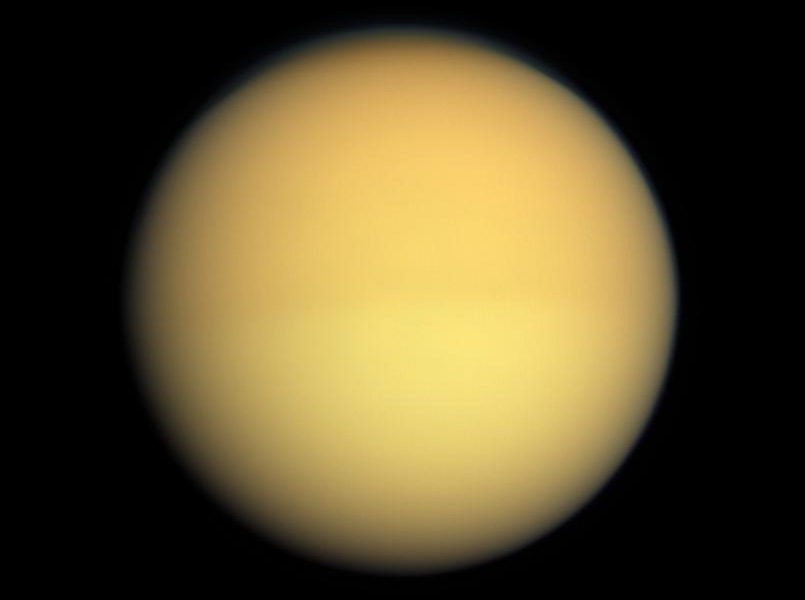 Titán en color natural mostrando una diferencia de tonalidad entre hemisferios debido a cambios estacionales en su atmósfera